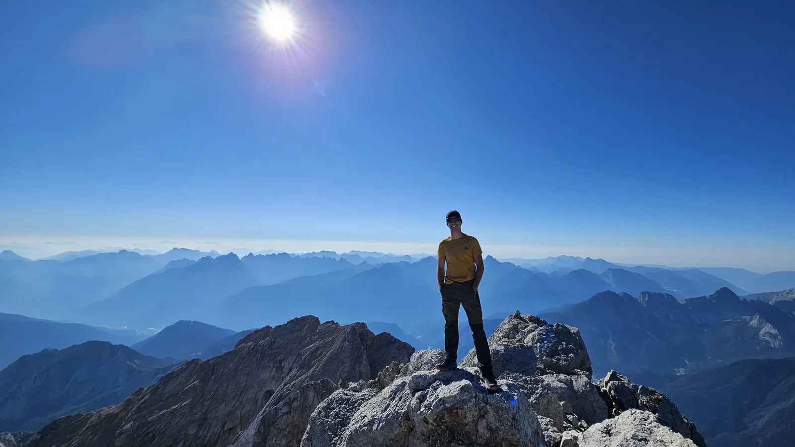 A hiker on a rocky summit with layers of mountains in the distance