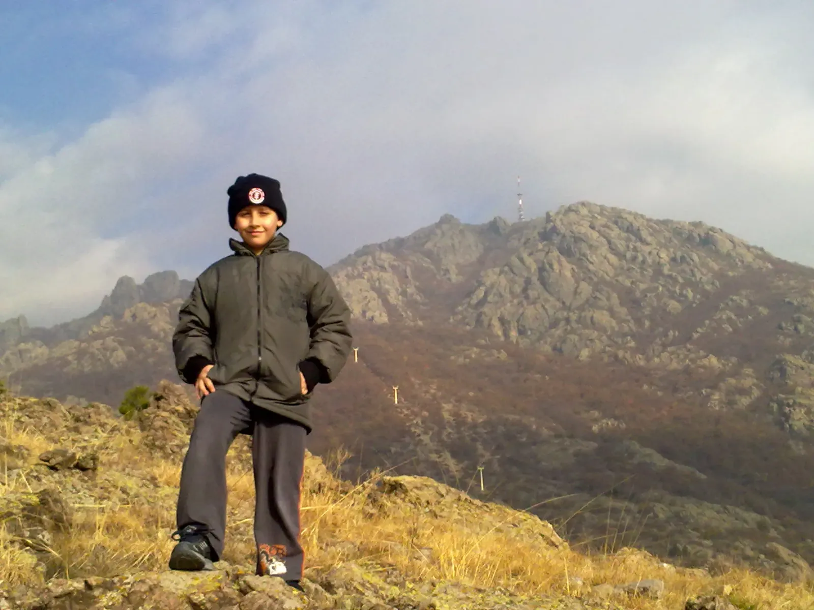 Lyuboslav Nemtsov as a child on a grassy hillside with rocky mountains behind him
