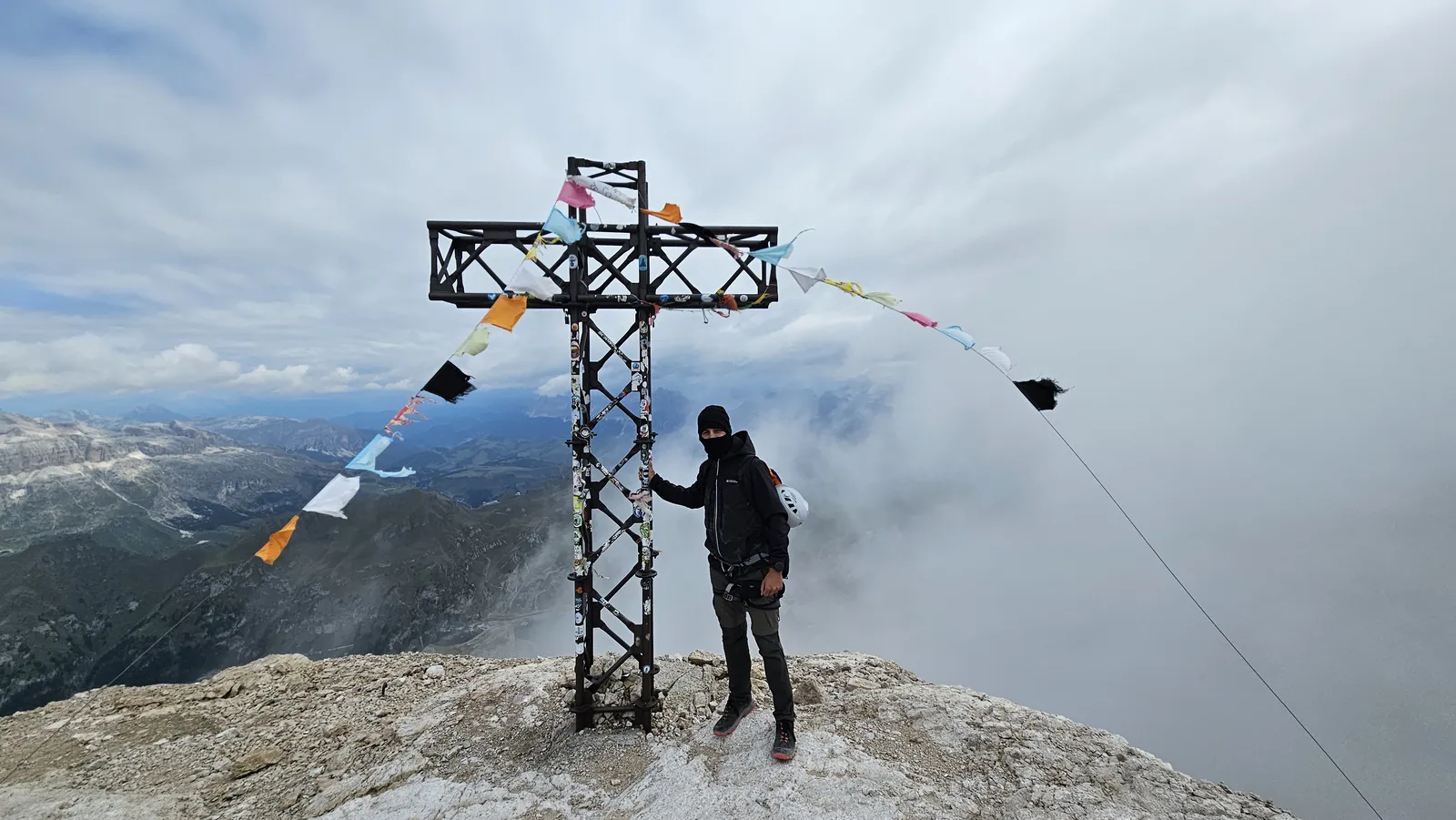 A hiker beside a summit cross on Marmolada under low cloud