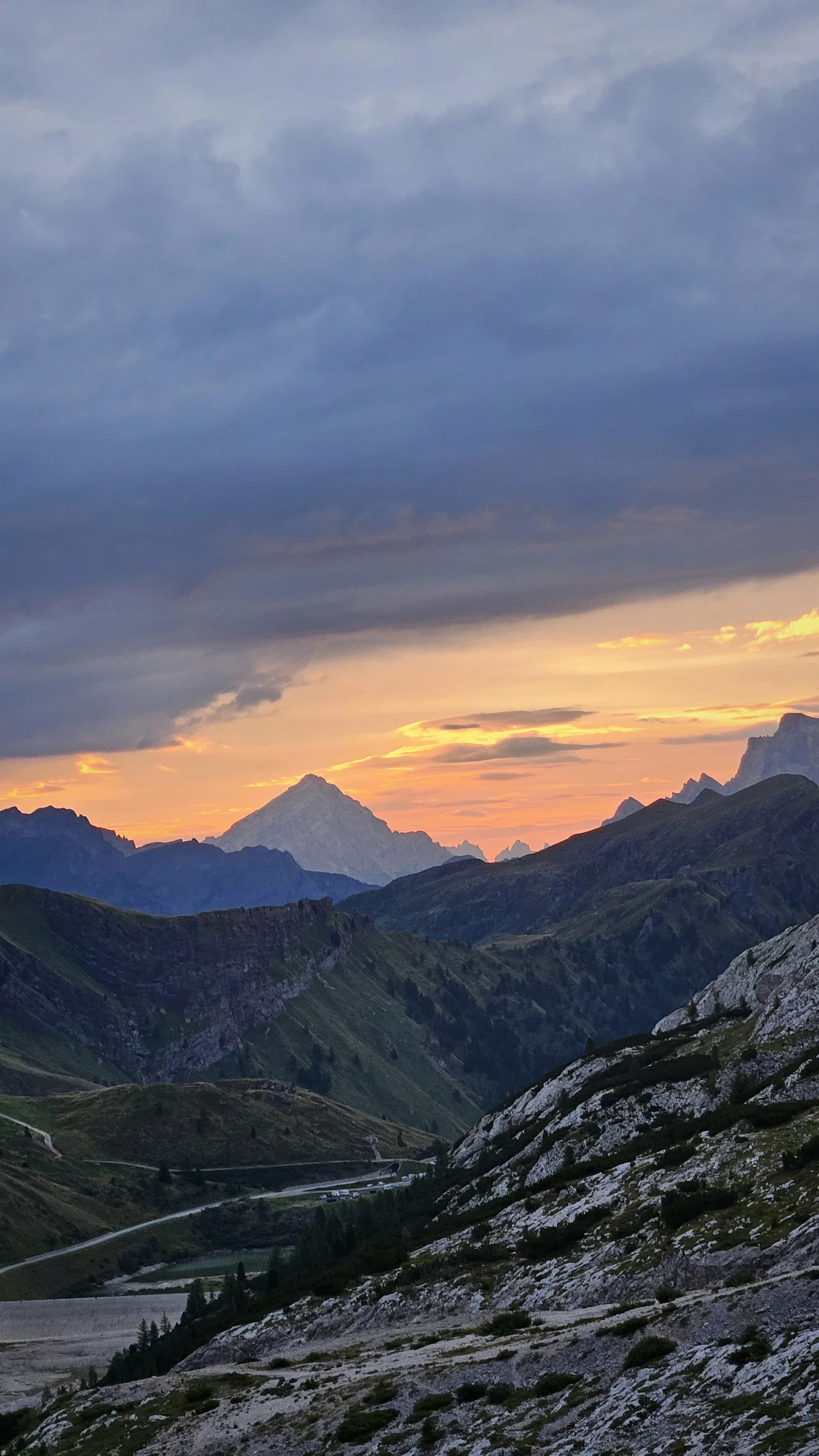 Dark mountain ridges beneath an orange sunset and heavy clouds