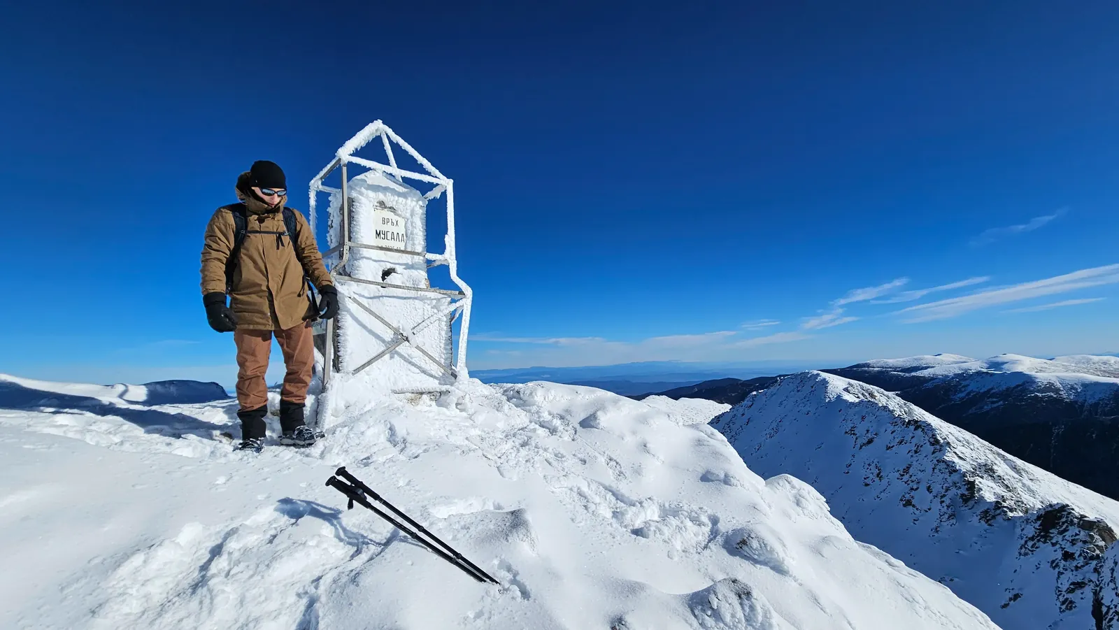 A hiker beside a summit structure on snow-covered Musala