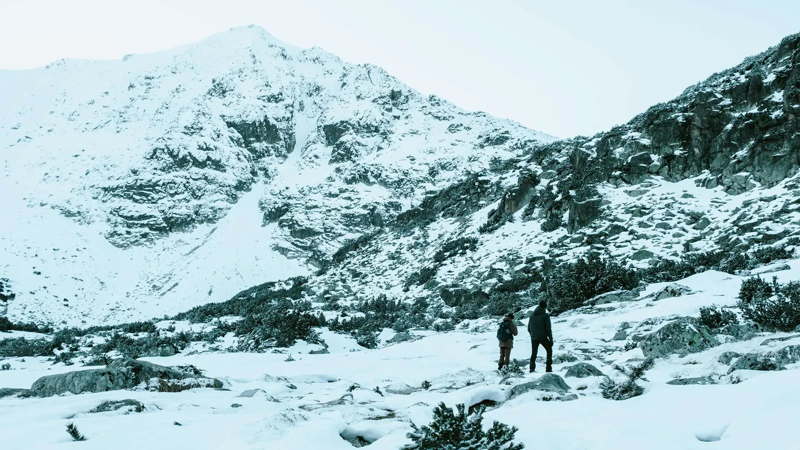 A hiker crossing a snow-covered valley below steep mountain slopes